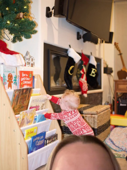 Pediatrician Dr. Em's son next to the Christmas stocking hanging on the wall in the background as an example of decorating safety